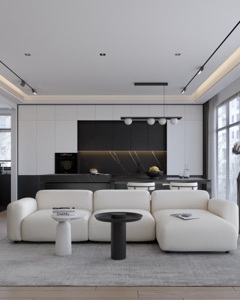 Minimalistyczny salon z jasną sofą, czarnym stołem kawowym i aneksem kuchennym w tle.